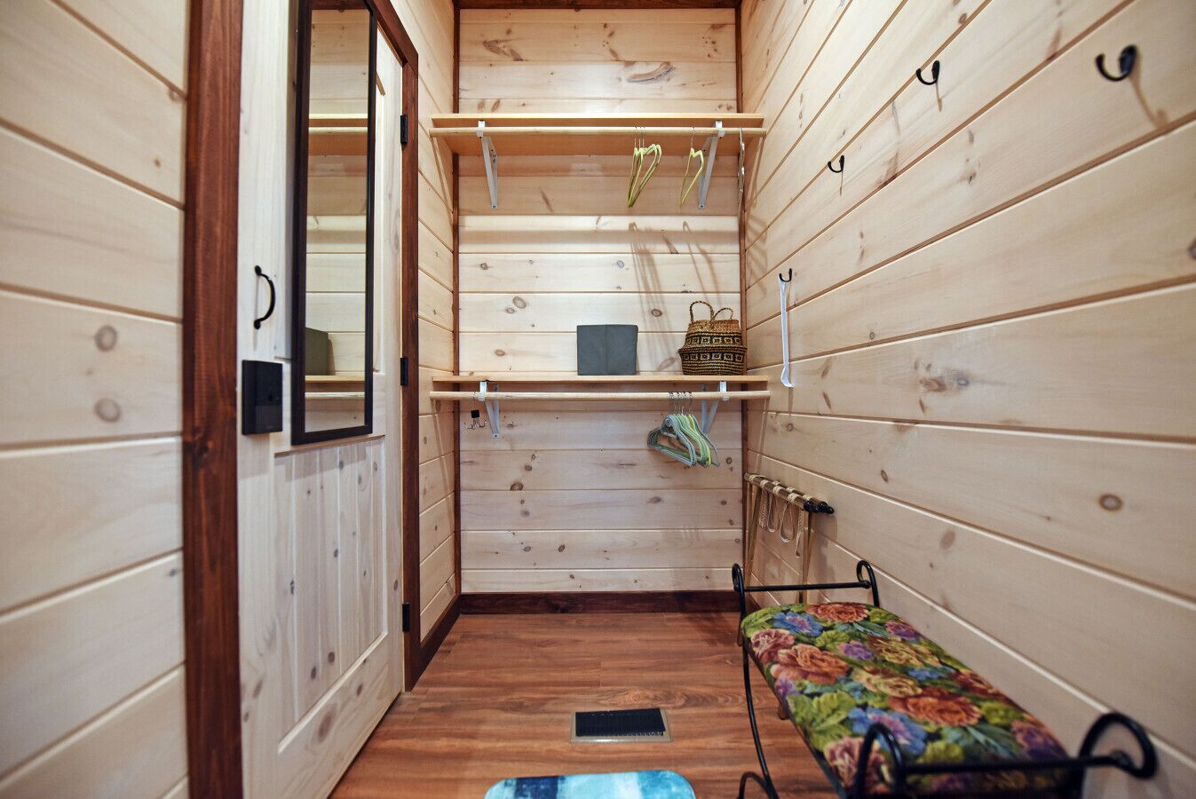 A narrow room with wooden walls, a bench, shelves with items, and a door.