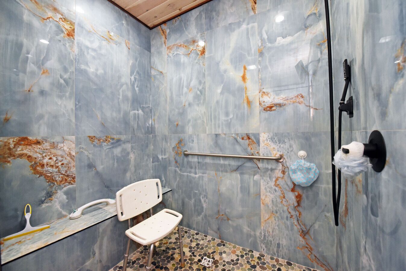 Un baño con ducha, un pasamanos, una silla blanca y una barra de apoyo.
