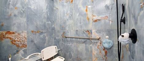 Un baño con ducha, un pasamanos, una silla blanca y una barra de apoyo.