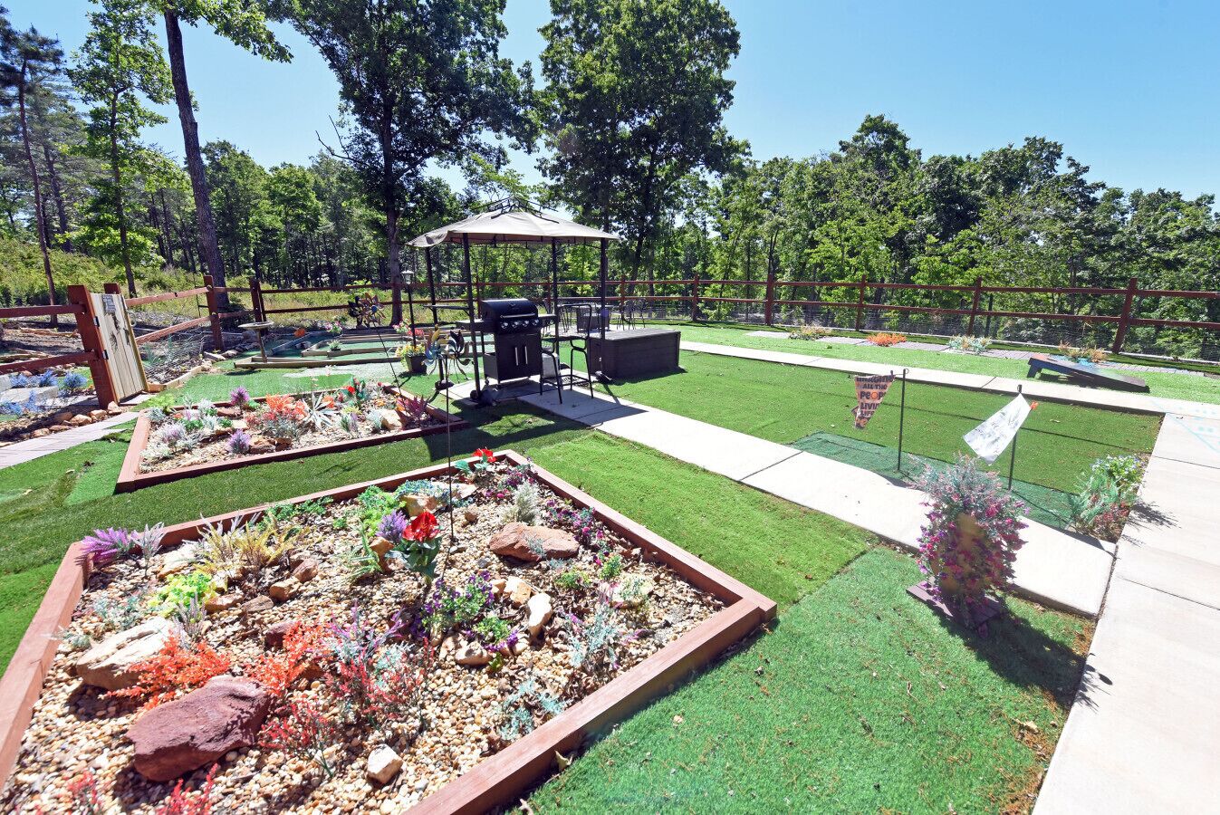 Un jardín ajardinado con un pabellón, una zona de barbacoa y diversas plantas.