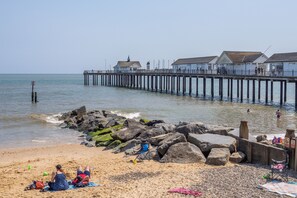 A beach with a pier extending into the water, rocky shoreline, and people relaxing on the sand. - Moles Meadow (4), Middleton (Middleton)