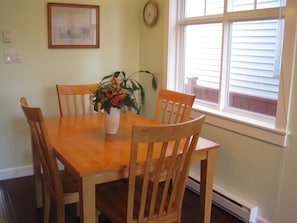 A dining table with chairs, a potted plant, a clock, and a window with blinds.