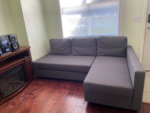 Ein Zimmer mit grauem Ecksofa, einer Holz-Unterhaltungseinrichtung mit Lautsprechern und einem Kamin.