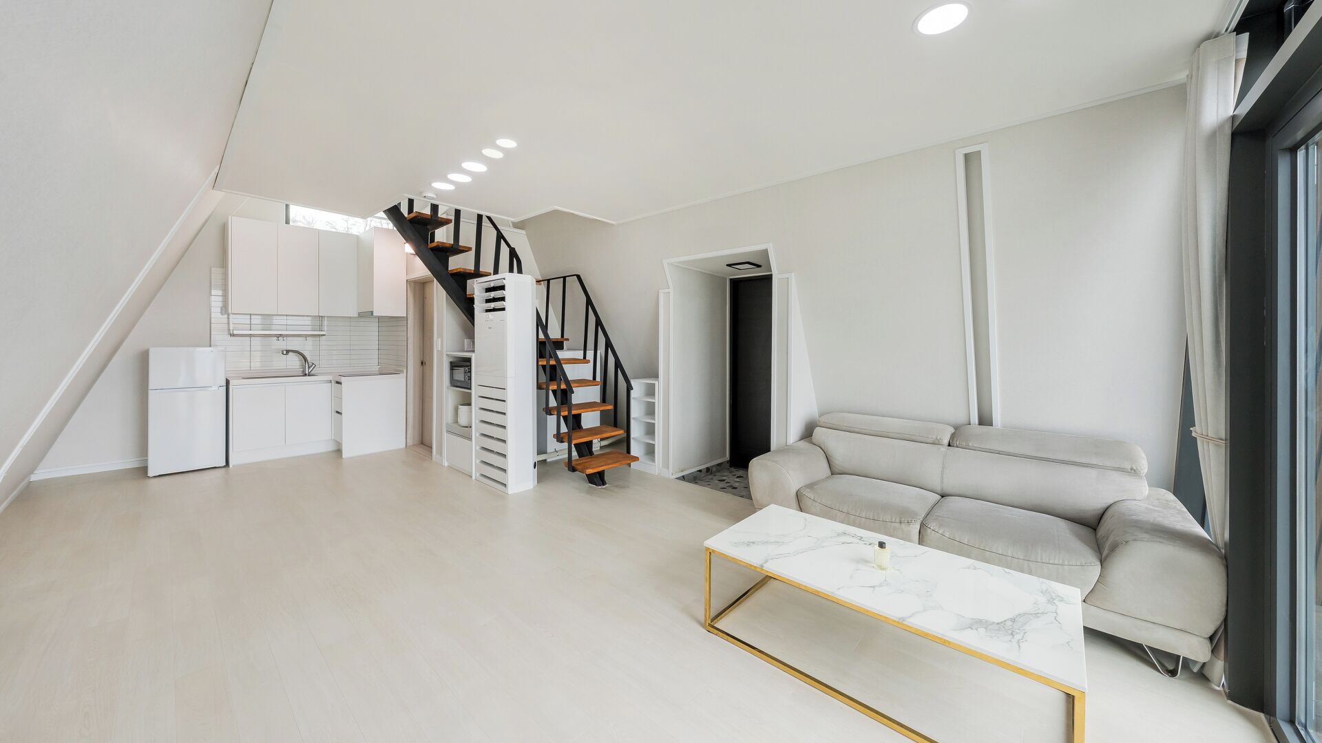 A modern living space with a kitchen, a staircase, a sofa, and a marble coffee table.
