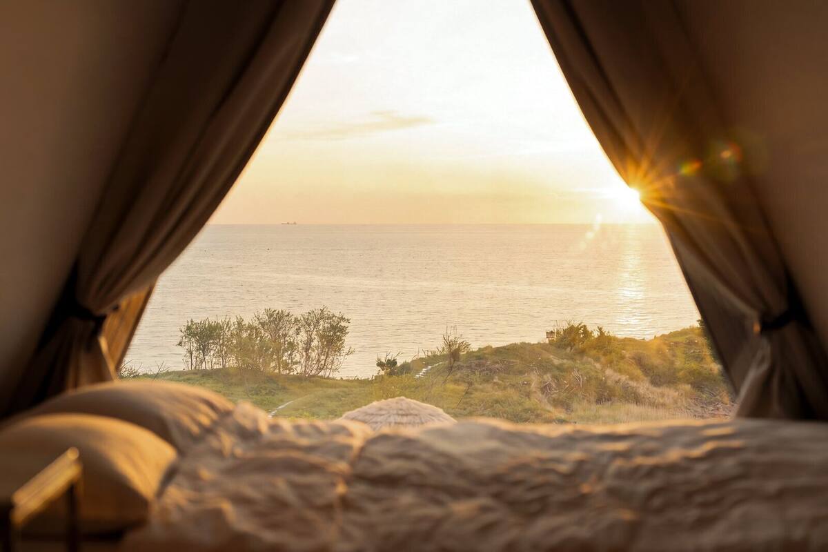 Una cama con vista al mar a través de cortinas.