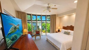 A hotel room with a bed, a desk with a TV, a chair, a ceiling fan, and a view of greenery outside. - Walk to Sandy Beach, Restaurants and Shops (Lahaina)