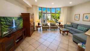 A living room with a TV, sofas, a coffee table, and a view of the outdoors. - Walk to Sandy Beach, Restaurants and Shops (Lahaina)