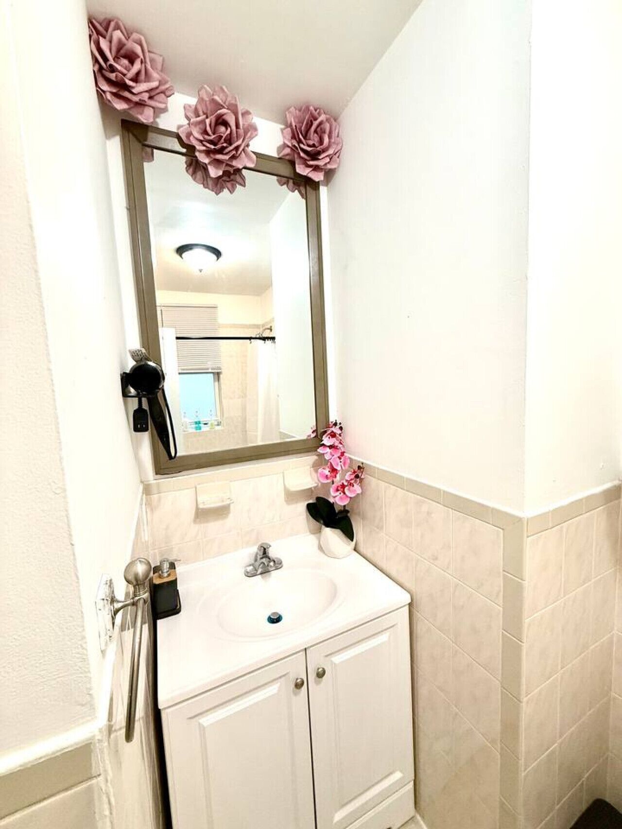 A bathroom with a white sink, a mirror with pink flowers, and a potted orchid.