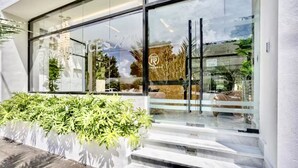 A modern building with large glass windows, a white exterior, and a small outdoor planter with green foliage. - Modern Luxury Retreat Residence XX11 La Esperilla (Santo Domingo)