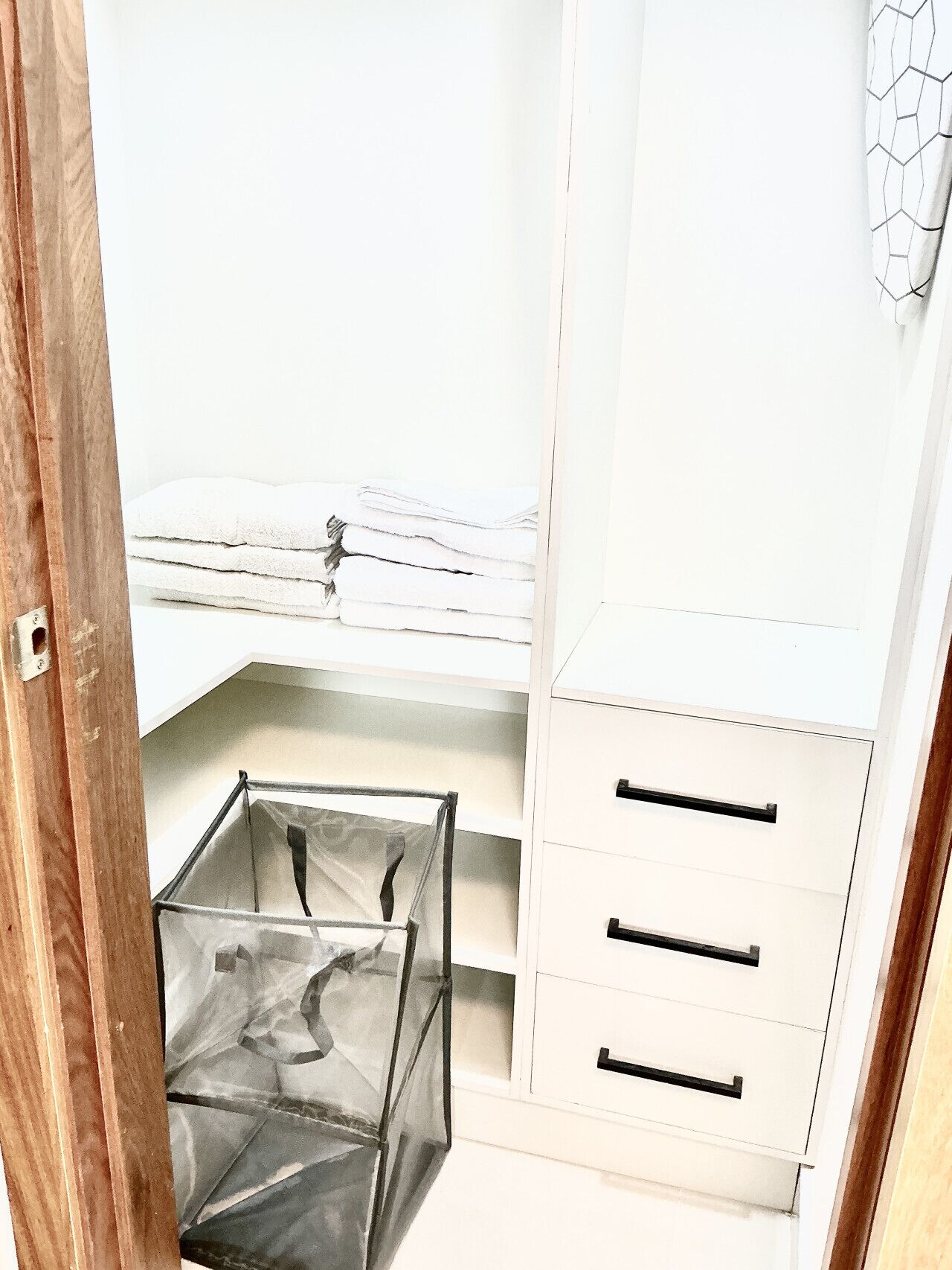 Een witte kast met een kledingroede, een opbergbox van netstof, en drie lades.