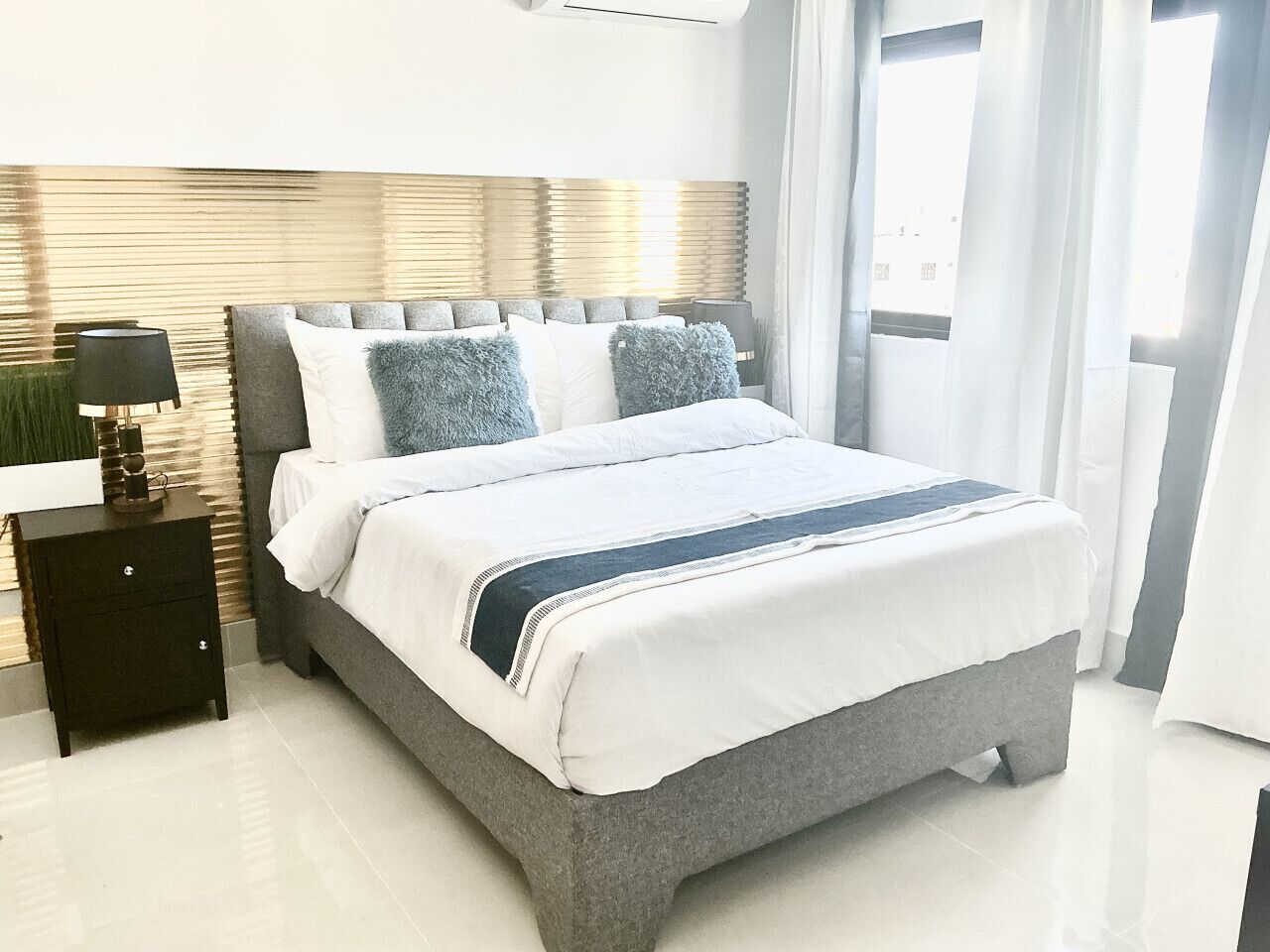 Une chambre à coucher moderne avec un grand lit, une table de chevet, une lampe et une fenêtre avec des rideaux.