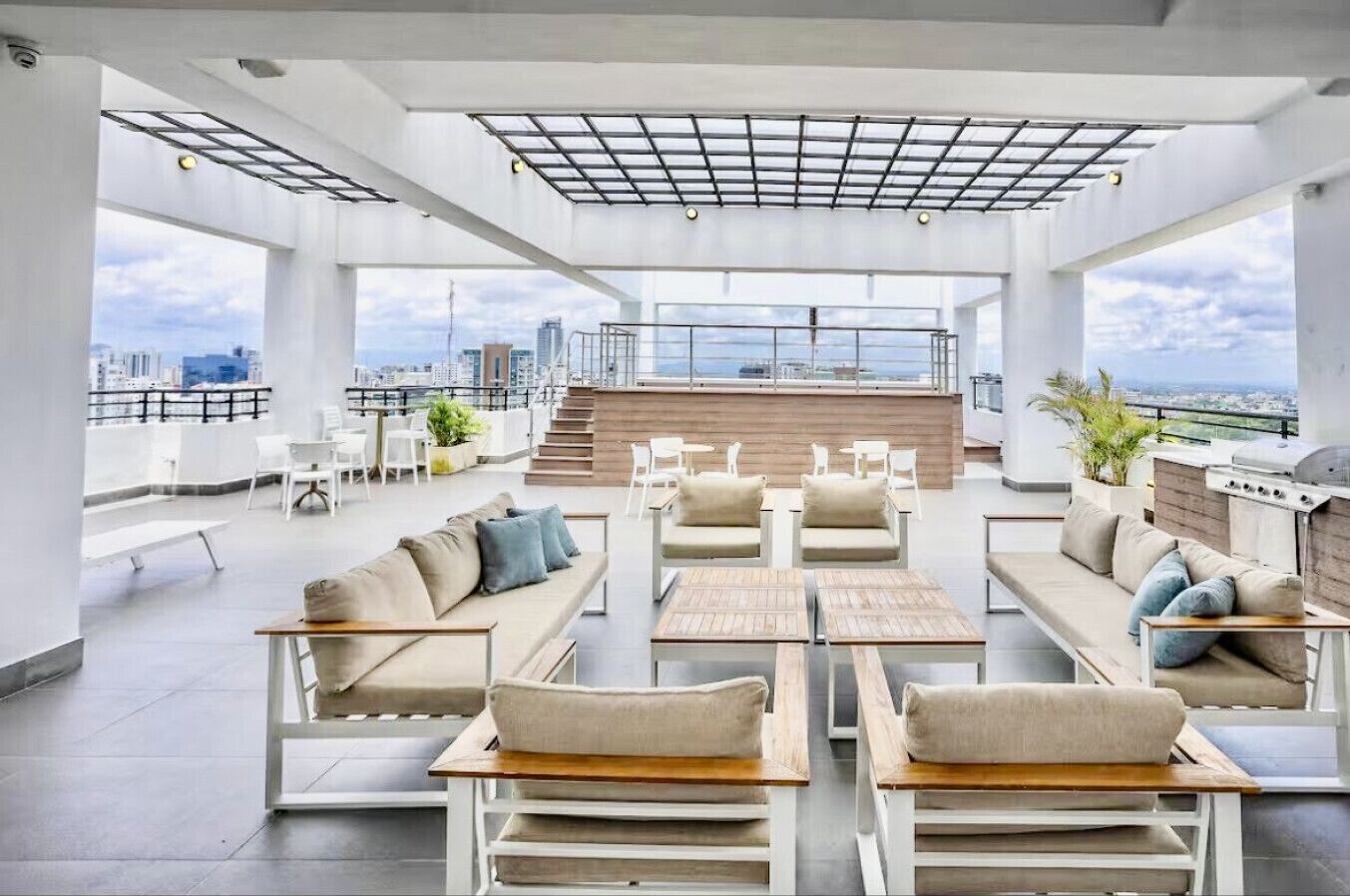 A rooftop lounge with sofas, tables, and a grill area, offering a city view.