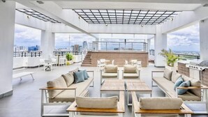 A rooftop lounge with sofas, tables, and a grill area, offering a city view. - Modern Luxury Retreat Residence XX11 La Esperilla (Santo Domingo)