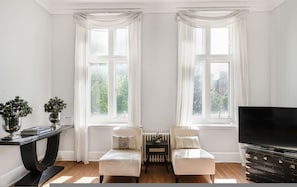 A room with two windows, a black TV stand, and two sofas. - Knightsbridge 2-bed Amazing Location (London)