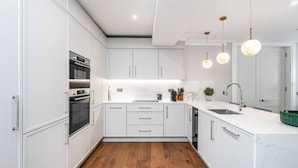 Una cucina moderna con mobili bianchi, forno integrato, lavello e illuminazione a sospensione.