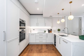 Eine moderne Küche mit weißen Schränken, einem Backofen, einer Spüle und Pendelleuchten.
