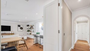 Een moderne keuken met witte kasten, een eetgedeelte met een houten tafel en stoelen, en een gang met een witte deur.