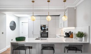 Een moderne keuken met een centraal eiland, hanglampen en een klok aan de muur.