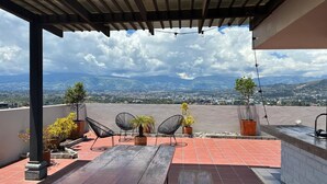 Eine Dachterrasse mit Holztisch, Stühlen, Topfpflanzen und Blick auf die Stadtlandschaft.