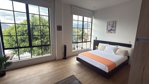 Ein Schlafzimmer mit großem Fenster, einem Bett, einem Nachttisch und einem an der Wand hängenden Bild.