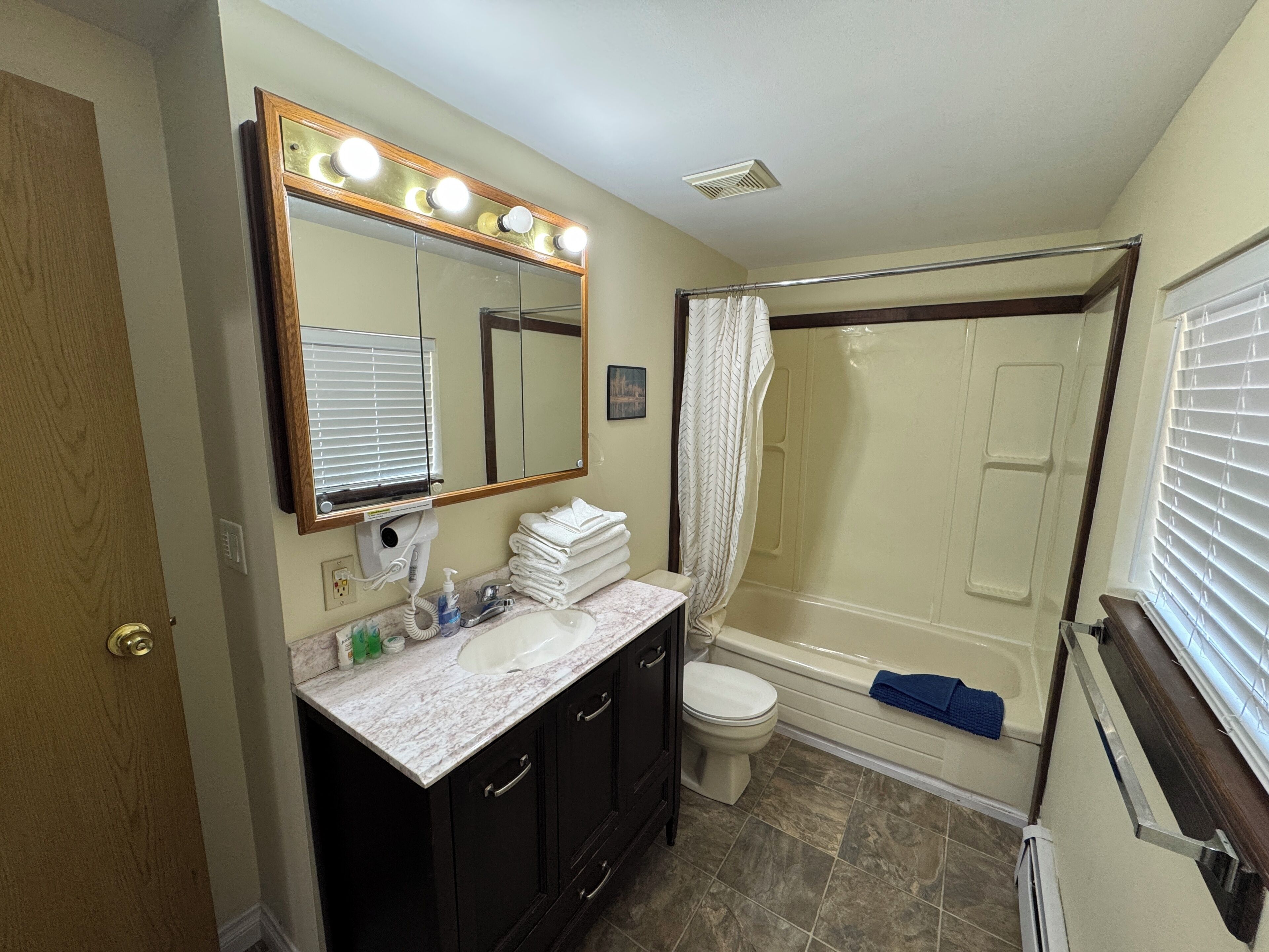 A bathroom with a vanity, a toilet, a shower, and a large mirror with lights.