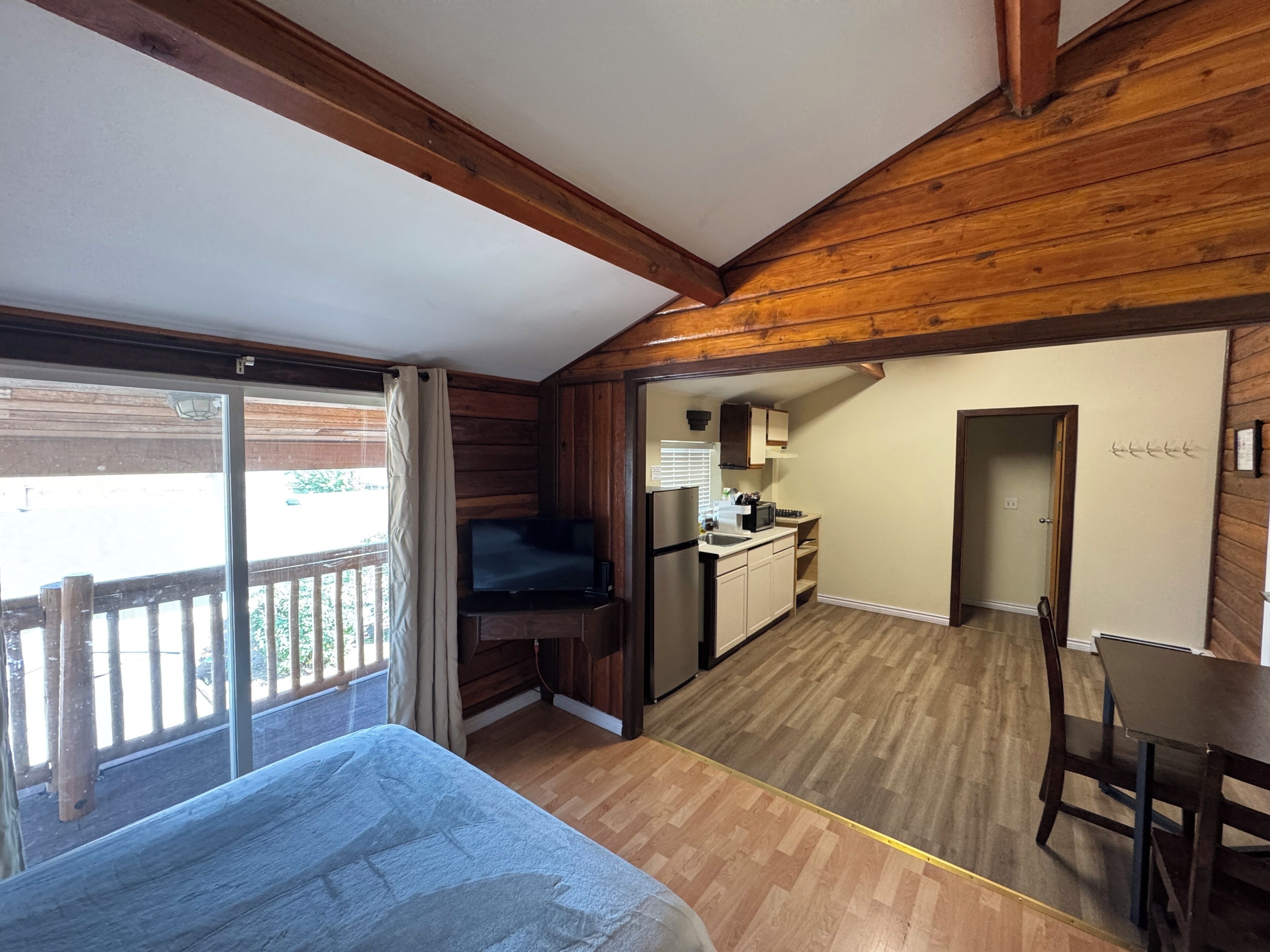 Una habitación con cama, televisión, zona de cocina y balcón.