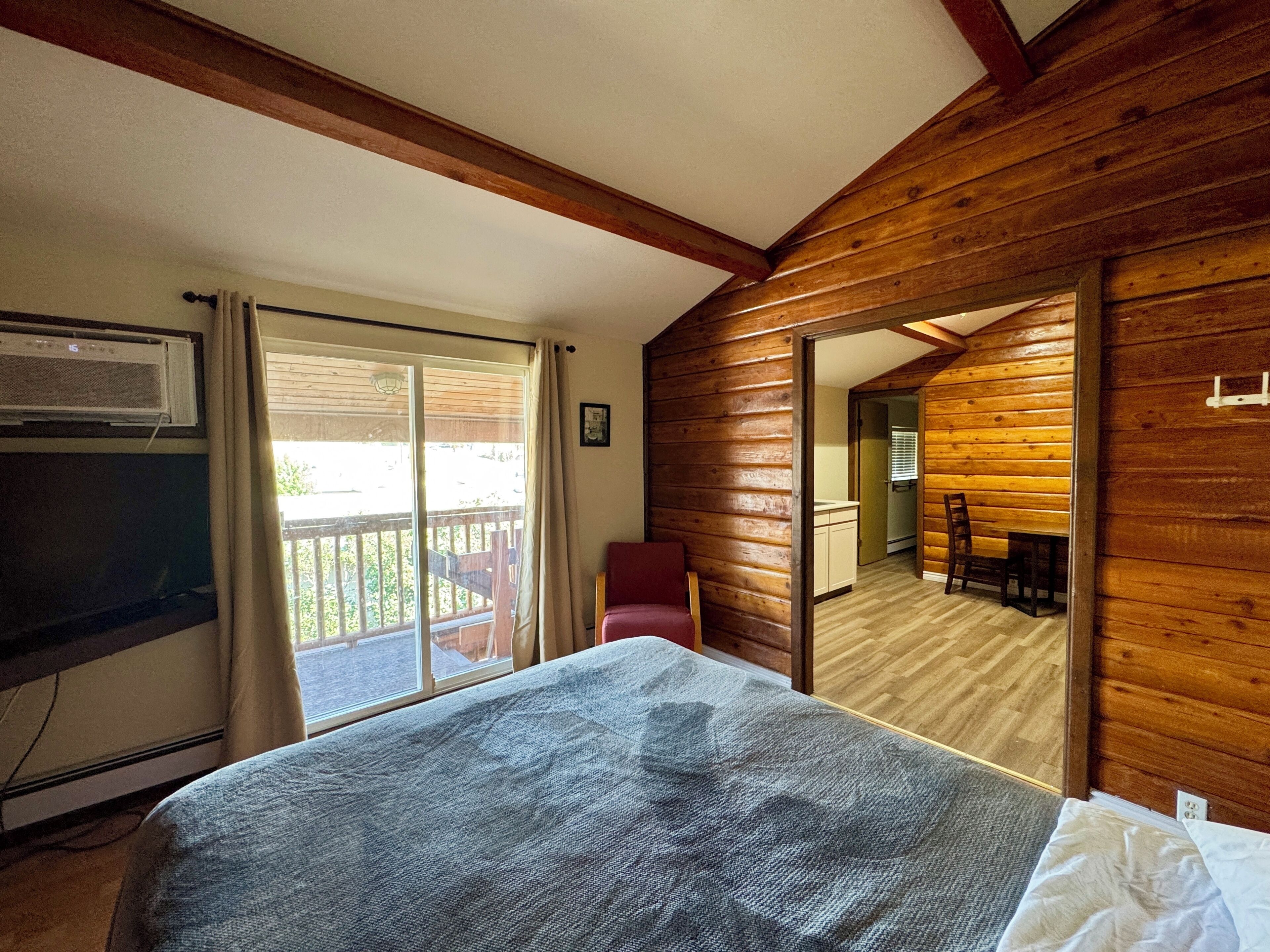 Una habitación con cama, televisión y puerta corrediza de vidrio que da a un balcón.