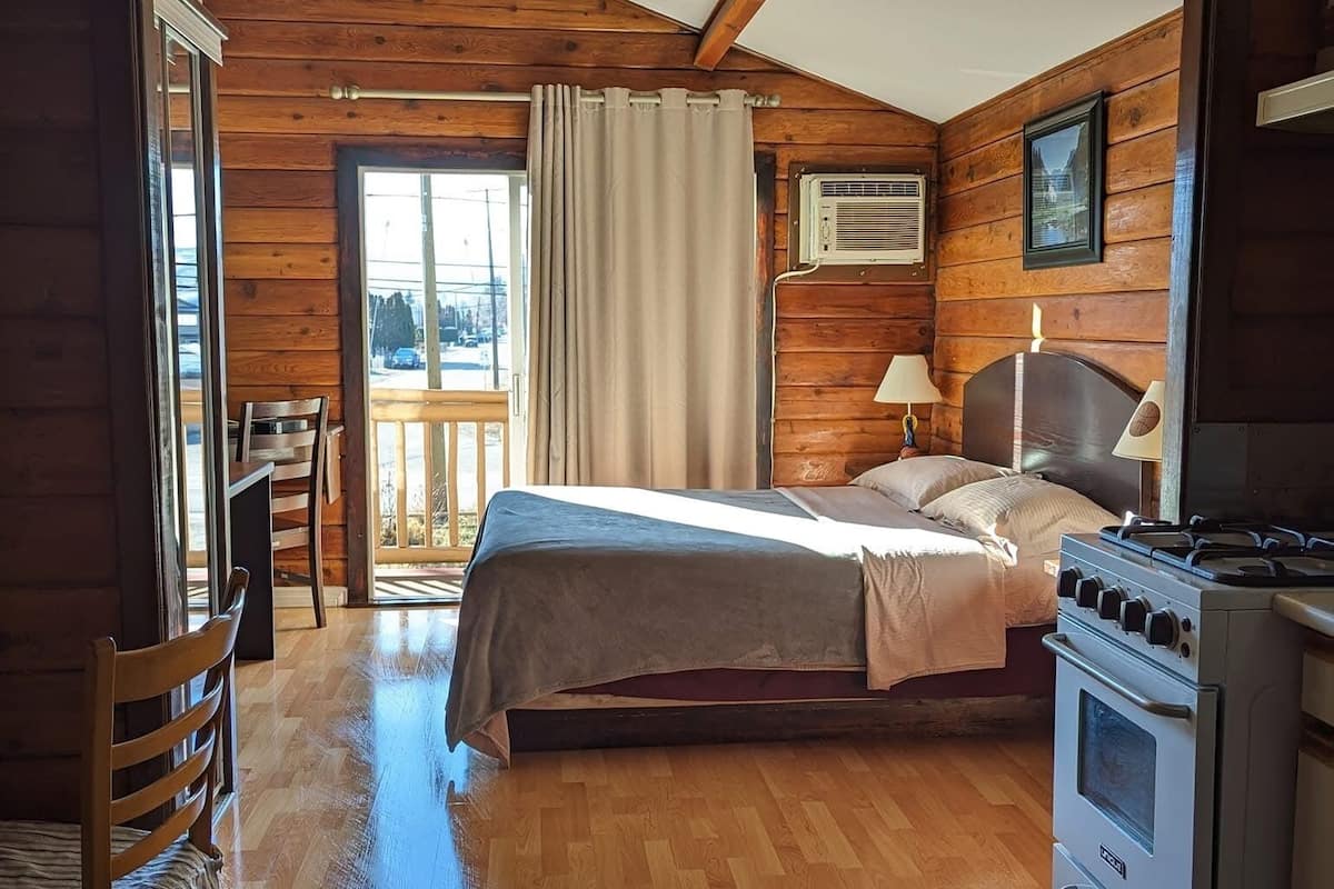 Un dormitorio de cabaña de madera con una cama, una silla, una mesa y una estufa.