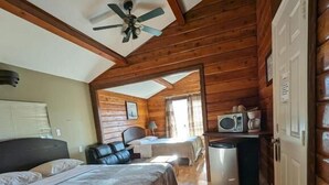 A wooden cabin with a bed, a desk, a chair, a ceiling fan, and a microwave. - Merritt Lodge Motel (Merritt)