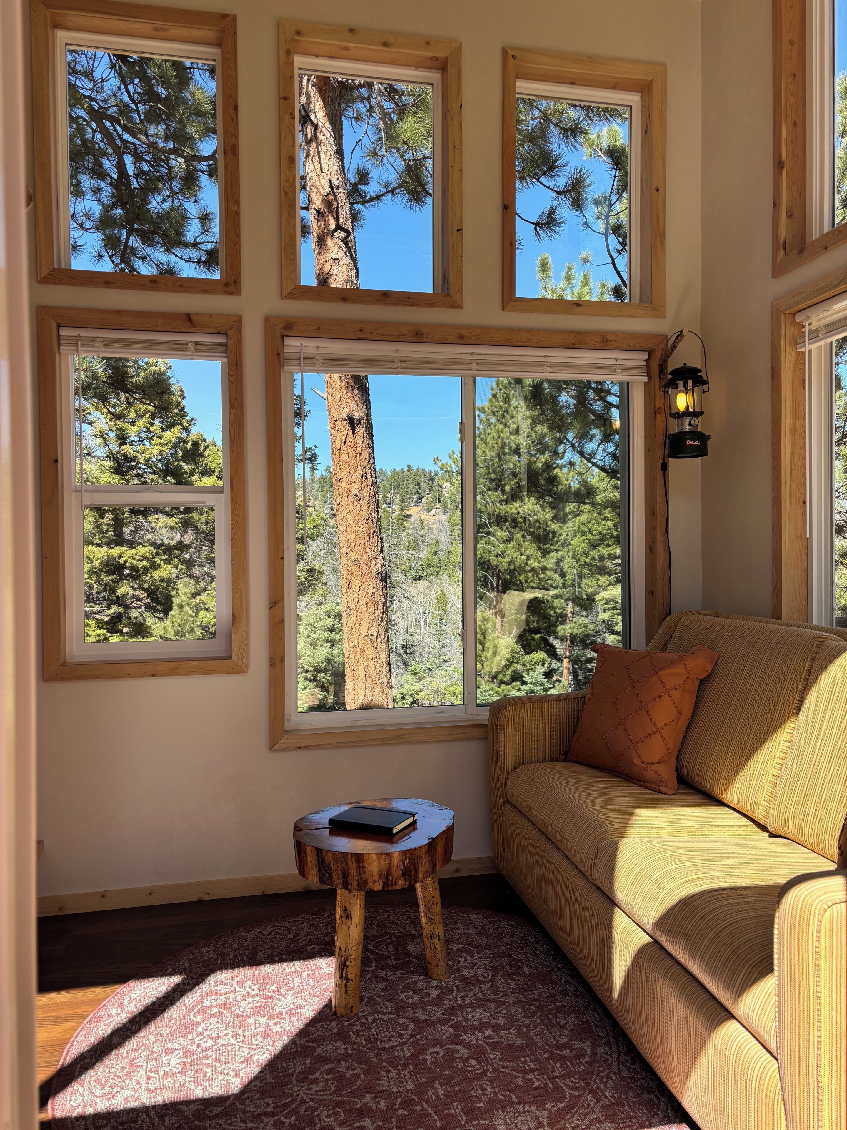 A room with multiple windows, a wooden floor, a sofa with a cushion, and a small wooden table with a book.