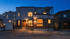 Uma casa moderna de dois andares, com telhado plano, janelas grandes e uma garagem visível.