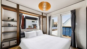 Quarto de hotel com uma cama grande, cabeceira de madeira, prateleira embutida, janela com cortinas e um candelabro.