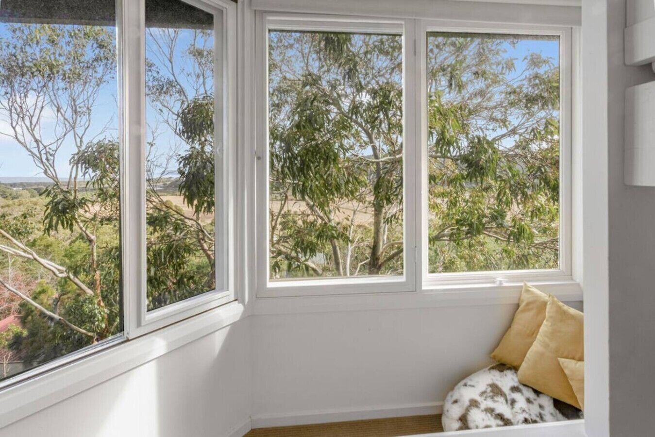 A room with a large window, a white wall, and a small seating area with cushions.