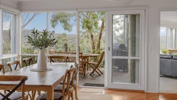 Un vaste espace dédié à la salle à manger, avec une table et des chaises en bois, de grandes fenêtres et une vue sur les arbres.