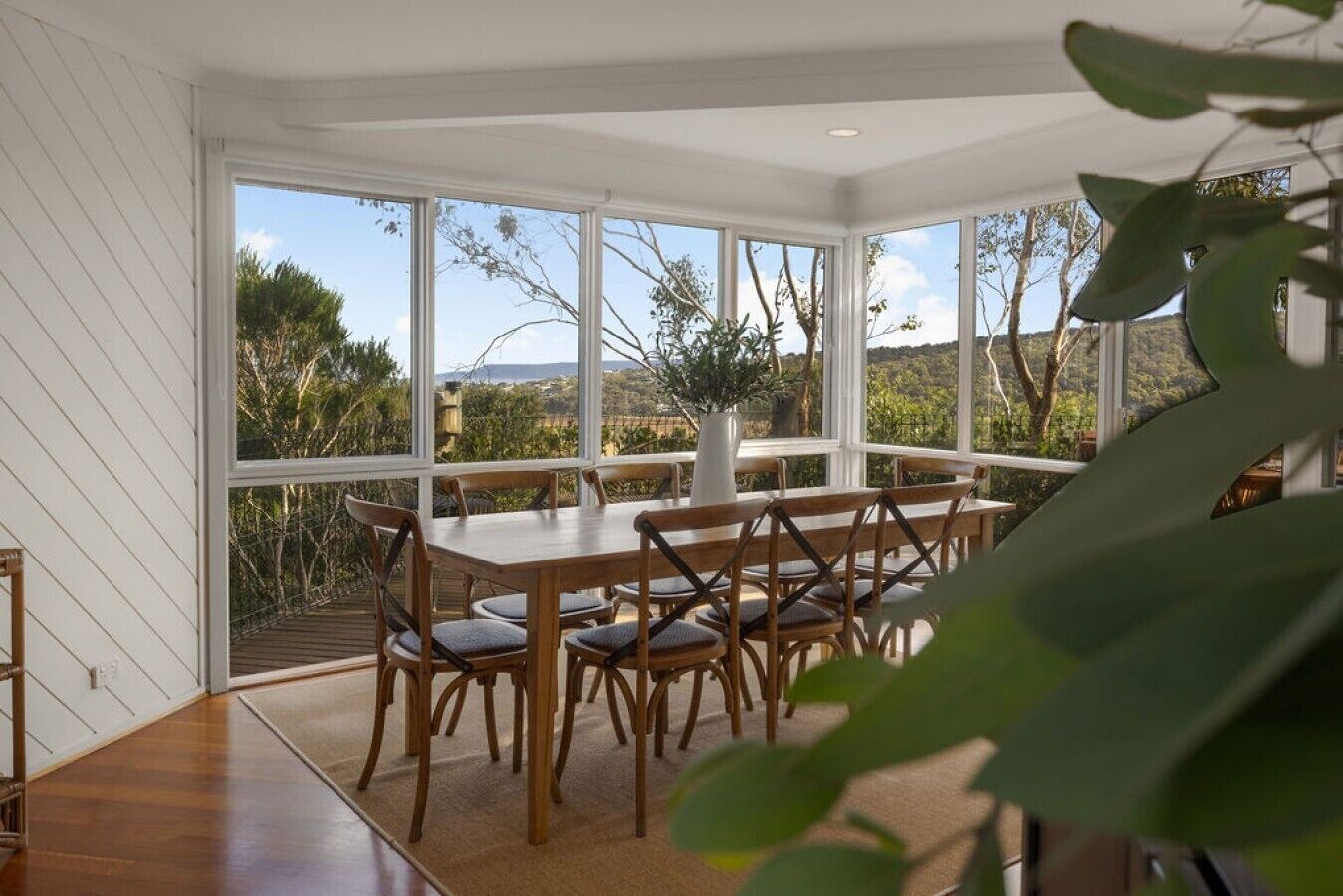 Un espace repas avec une table et des chaises en bois, de grandes fenêtres et une vue sur l’extérieur.