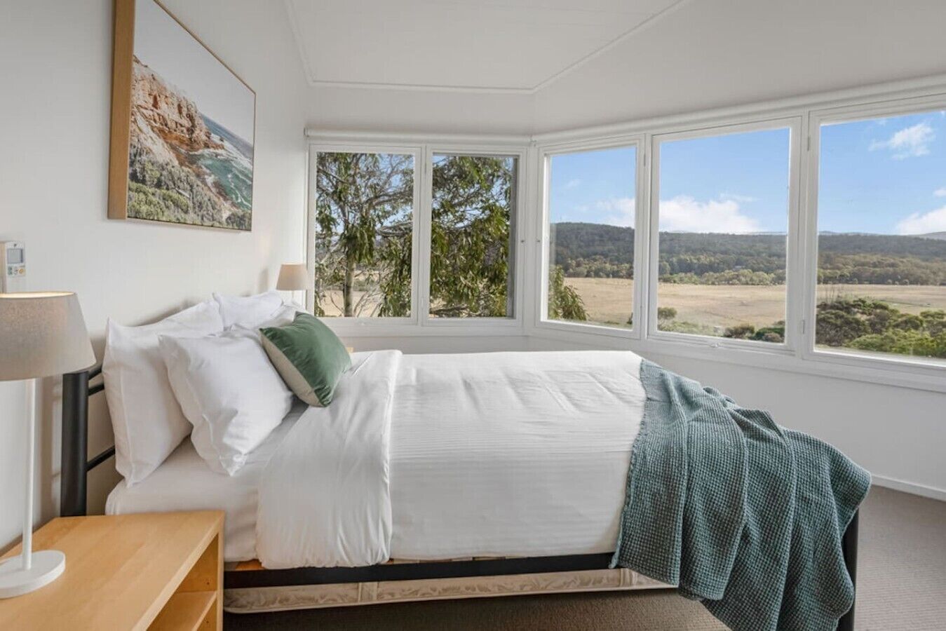 A bedroom with a bed, a bedside table, a lamp, and a view of the outdoors.