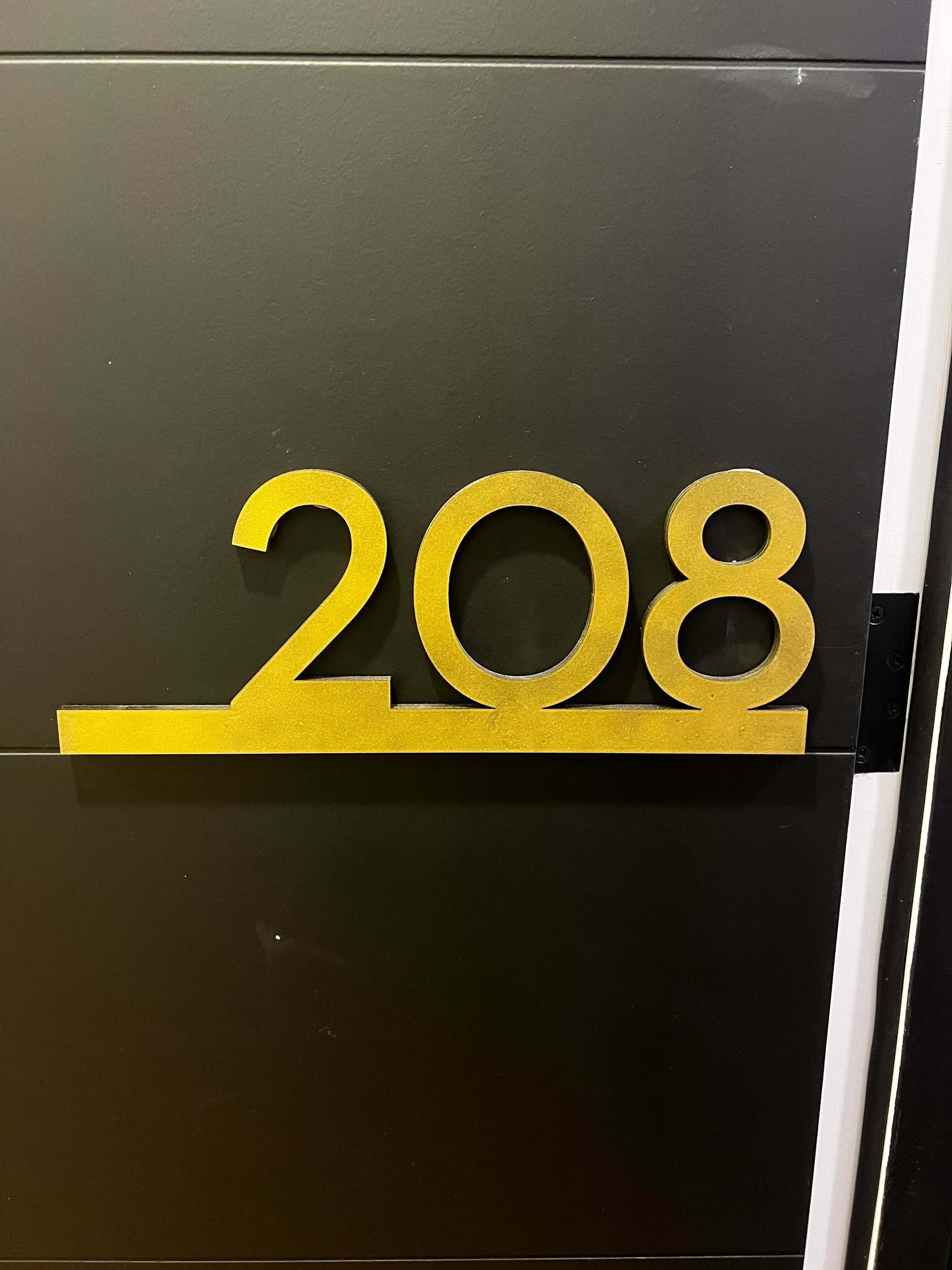 A black door with a gold number '208' sign.