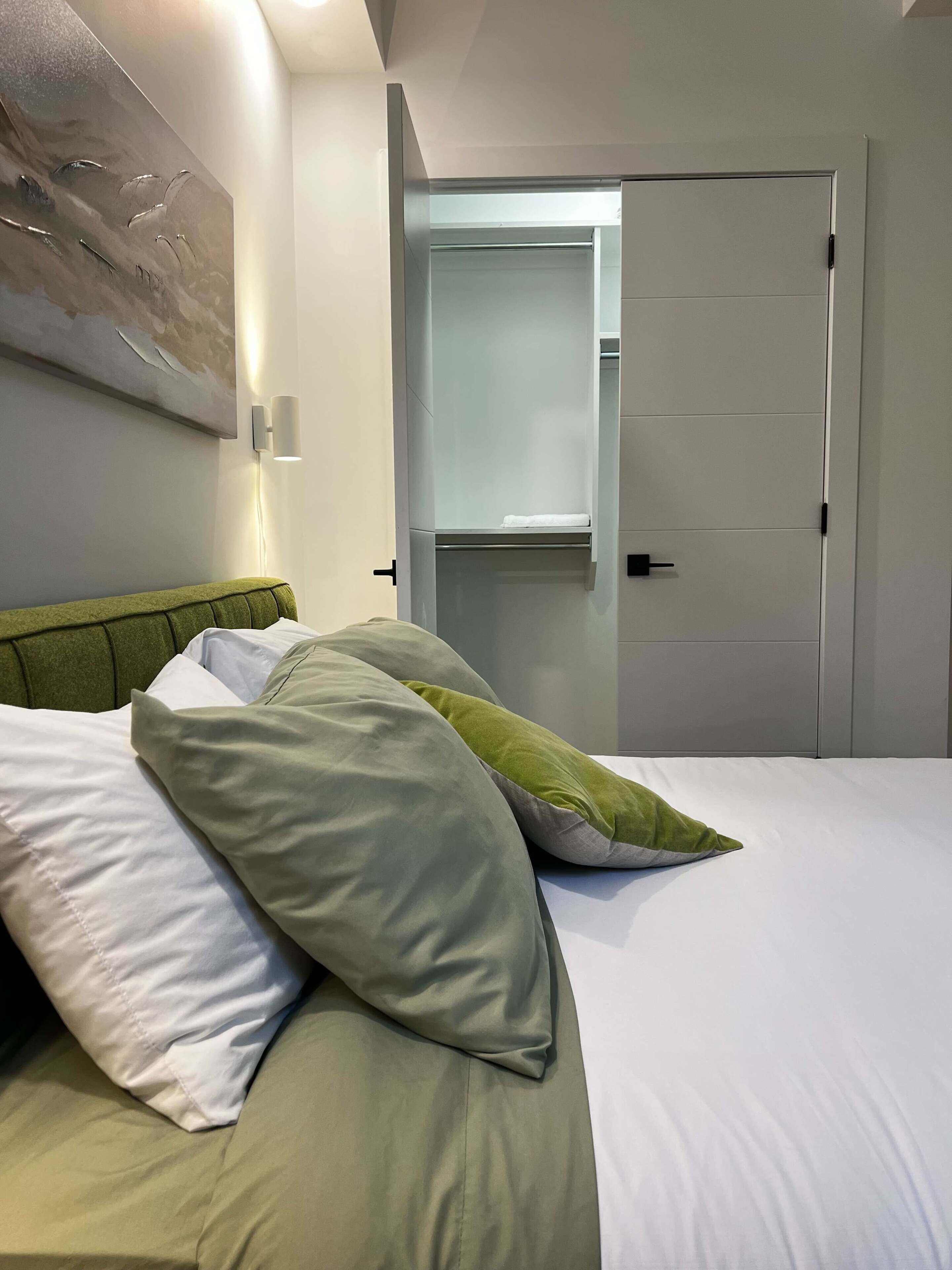 Een hotelkamer met een bed, nachtkastje, een aan de muur bevestigde lamp en een deur.