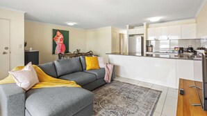 A modern living room with a grey sofa, a patterned rug, and a kitchen area with white cabinets and a stainless steel refrigerator. - Quiet Family Stay in Albion | Parking & City Views (Albion)