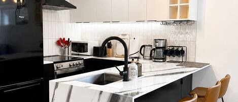 A modern kitchen with a marble island, black appliances, and pendant lighting.