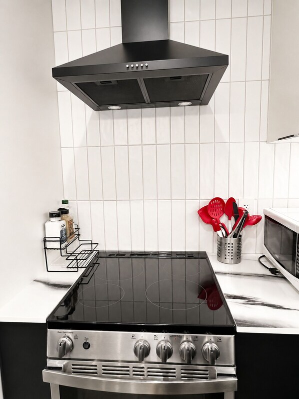 A kitchen with a black stove, white tiled backsplash, and a stainless steel range hood. - New, Sunny Two Bedroom Garden Suite in Prime Kitslano (Vancouver)