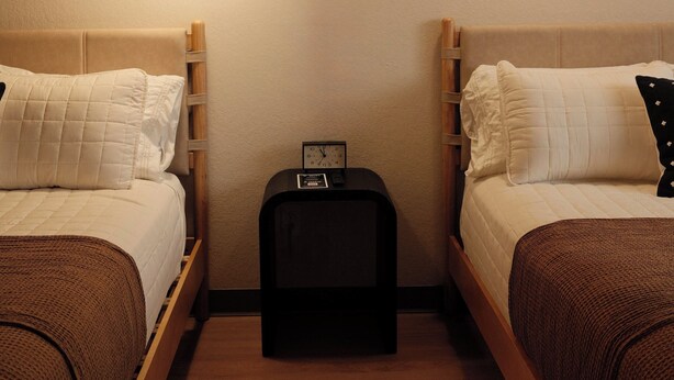 Een tweepersoonskamer met twee bedden, een nachtkastje, een lamp en een klok.