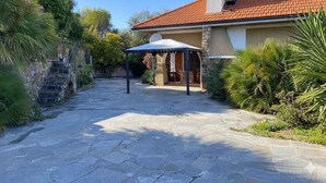 A stone pathway leading to a house with a red-tiled roof, a covered outdoor seating area, and lush greenery. - Villa with air conditioning, pool and terrace with sea view (Imperia)