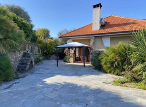 A stone pathway leading to a house with a red-tiled roof, a covered outdoor seating area, and lush greenery. - Villa with air conditioning, pool and terrace with sea view (Imperia)