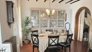 A dining area with a table set for four, a chandelier, and a view through a window with glass doors. - Villa with air conditioning, pool and terrace with sea view (Imperia)
