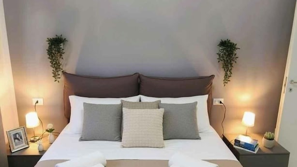 Una cama bien hecha con almohadas, una lámpara de noche y una planta pequeña a cada lado.
