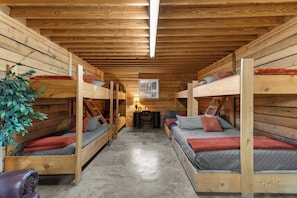 Una cabaña con paredes y pisos de madera, literas, una mesa pequeña con una lámpara y una ventana.