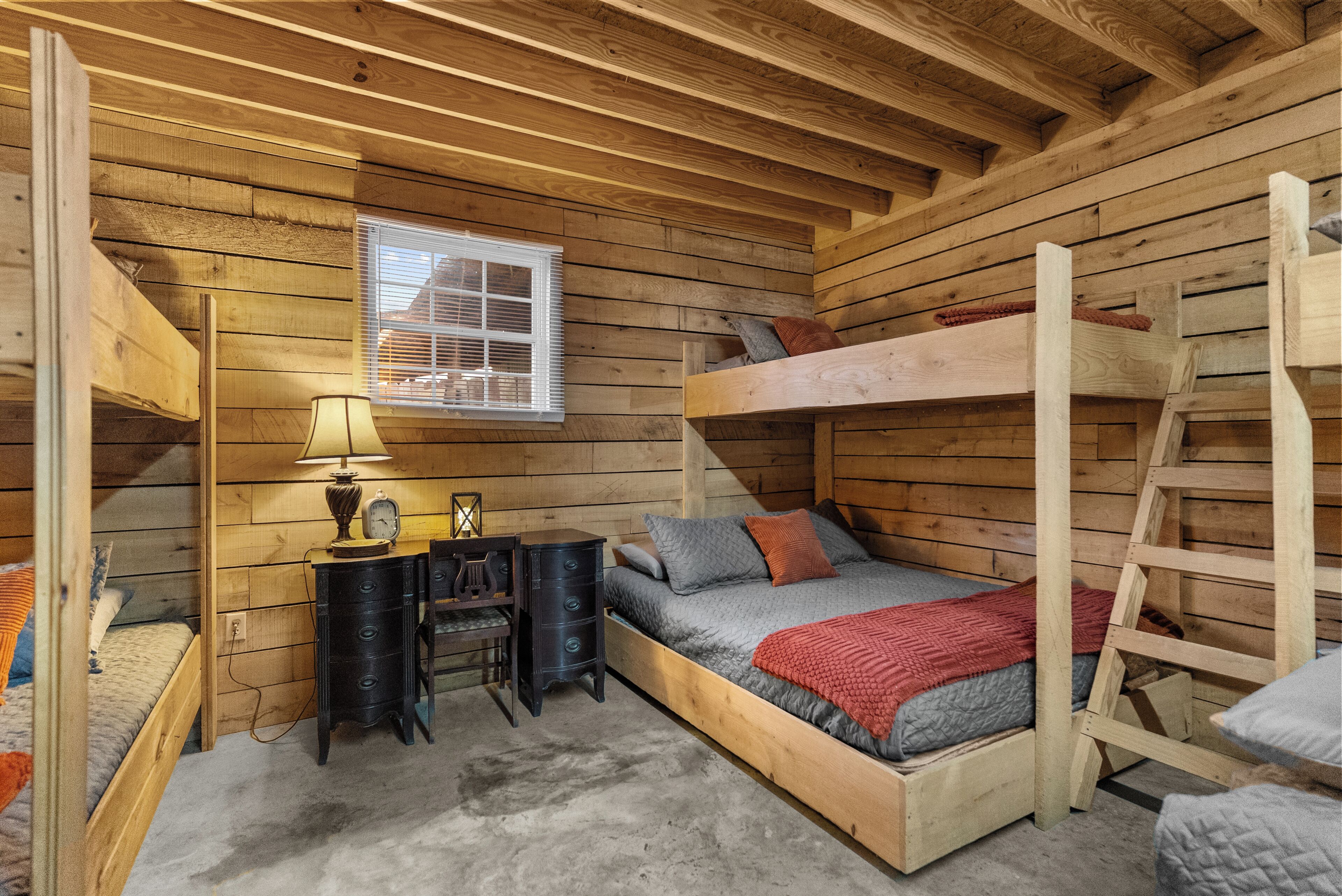 Une petite pièce de cabane en bois, avec des lits superposés, un bureau avec une lampe et une fenêtre.