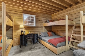 A compact wooden cabin room with bunk beds, a desk with a lamp, and a window.