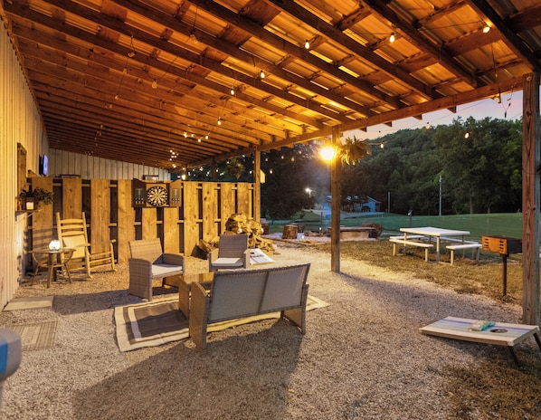 An outdoor covered patio with seating, a dartboard, and a television.